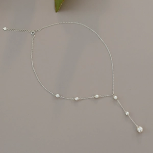 Macro shot of silver Y-shaped freshwater pearl necklace on a neutral minimal background