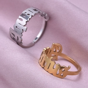 Detailed close-up of hollowed-out Gothic letter rings on soft pink satin fabric background
