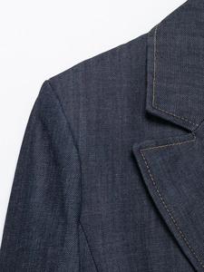 Dettaglio macro della spalla della giacca in denim blu scuro con cuciture a contrasto