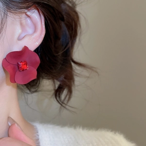Close-up of elegant red flower stud earrings with a central rhinestone worn by a model