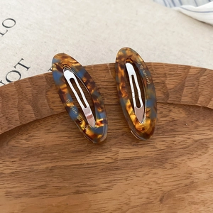 Detail of tortoiseshell acetate oval hair clips with gold lettering on a wooden tray