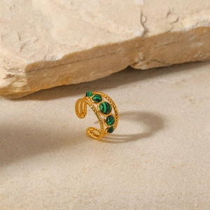 Detail of gold hollow open ring with green malachite stones on beige stone background