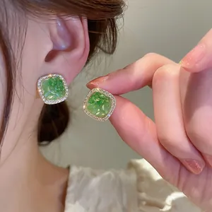 Detailed close-up of square green crystal earrings with a shimmering pavé diamond halo