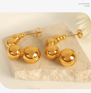 Detail shot of golden bean earrings on a stone base featuring a high-gloss metal finish