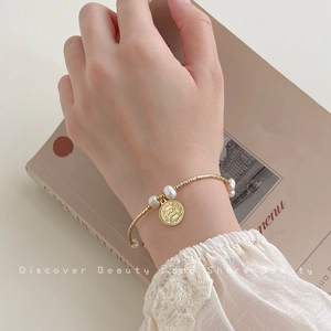 Elegant baroque pearl bracelet with vintage coin pendant worn on a wrist over a book