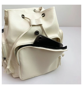 Detailed view of cream backpack front zipper pocket with phone showing storage capacity