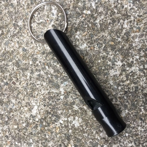 Matte black aluminum survival whistle with key ring on a rugged outdoor stone surface