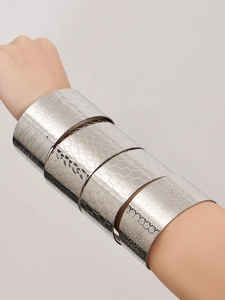 Détail de larges bracelets argentés avec diverses textures portés sur le bras d'un mannequin