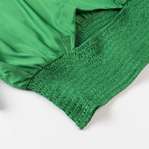 Detailed view of elastic smocked waist on a green satin short-sleeve crop top