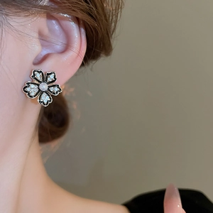 Detail of vintage flower stud earring with black enamel edges and pearl center on ear