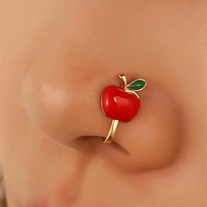 Close-up of a U-shaped gold non-piercing nose ring featuring a red apple enamel design