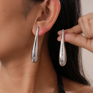 Close-up of model wearing silver teardrop earrings with a high-polish metallic finish