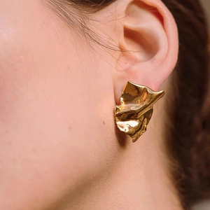 Macro shot of gold irregular wrinkled square earrings worn on model earlobe