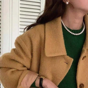 Close-up of elegant French vintage pearl necklace and earrings on model wearing camel coat