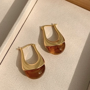 Detailed macro view of golden U-shaped hoop earrings with amber brown resin charms