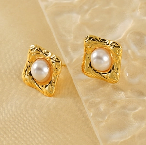 Detailed close-up of 18K gold textured square pearl stud earrings on gold silk