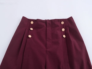 Detail view of burgundy high-waisted trousers with decorative gold buttons and texture