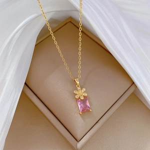Macro view of golden necklace featuring a pink rectangular gemstone and floral charms