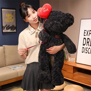 Close-up of a large black curly plush teddy bear with a red heart balloon for gifting