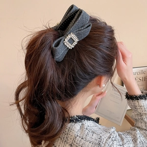 Detail view of a dark grey tweed bow hair claw clip with a sparkling rhinestone center buckle