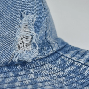 Detailed macro view of distressed light blue denim bucket hat with frayed hole and stitching