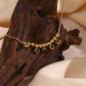 Detail of 18K gold plated anklet with green diamond pendants on dark textured wood
