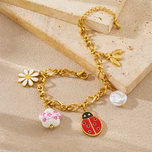Gold charm bracelet with daisy, ladybug and honeybee pendants on stone background
