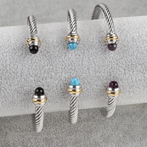 Macro detail of twisted cable bangles with colorful gemstones on a gray velvet jewelry roll