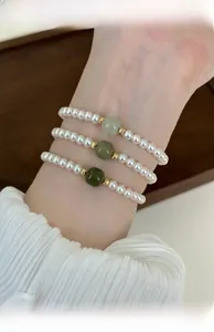Detailed view of layered Hetian jade and pearl beaded bracelets set on a female wrist