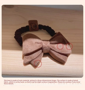 Macro detail of brown plush bow hair tie featuring a leather smiley face charm tag