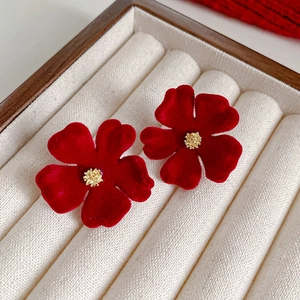 Gros plan de boucles d'oreilles fleurs en velours rouge avec centres dorés sur socle