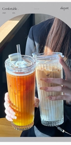 Detail of vertical ribbed glass coffee cup with white lid and straw held in hands
