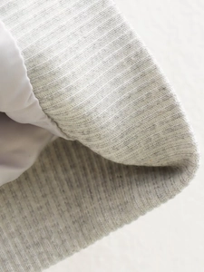 Vue macro de la texture en maille côtelée gris clair sur le poignet et l'ourlet de la veste
