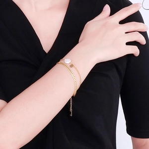 Double-layered gold bracelet with a white pearl and pendant on a model's wrist