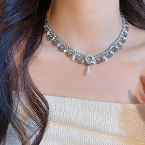 Close-up of a woven lace pearl choker with a blue gemstone and teardrop pearl pendant