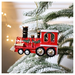 Detail of red Christmas train ornament hanging on snowy pine branch with bokeh lights