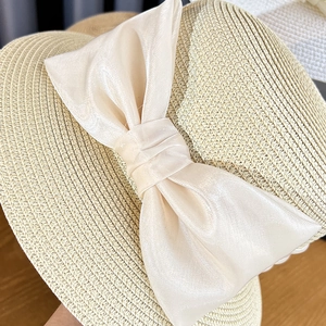 Detail of elegant beige straw hat featuring a large satin bow with smooth silky texture