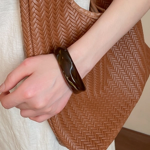 Close-up of a wide translucent brown acrylic wavy bangle worn on wrist for a chic look