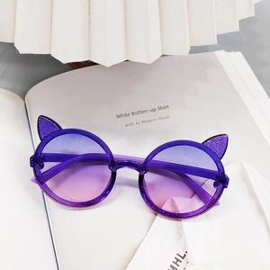 Detail of glitter purple cat-ear sunglasses for kids with gradient lenses on a magazine