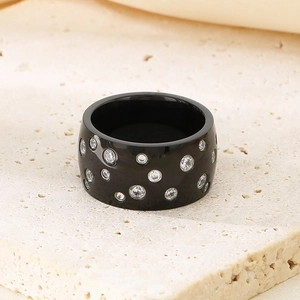 Macro view of wide black ring with sparkling round stones on beige stone surface