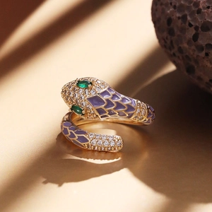 Detail view of gold snake ring featuring purple enamel scales and green gemstone eyes