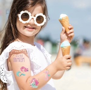 Glitter mermaid and unicorn temporary tattoos for kids shown on a girl's arm at the beach