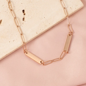 Detail of rose gold paperclip chain necklace with two rectangular bar pendants on stone