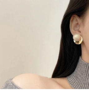 Close-up of elegant gold twisted hoop earring with a large pearl on a model