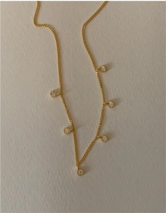 Detailed view of a gold dainty necklace with seven circular cubic zirconia stones