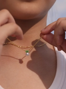 Detail of elegant gold necklace featuring white pearl and green crown pendant on neck