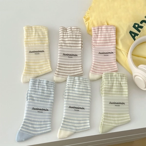 Six pairs of striped cotton crew socks in pastel colors laid out with lifestyle props