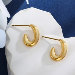 Elegant gold C-shaped stainless steel hoop earrings on white stone base with blue backdrop