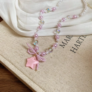 Macro detail of pink bow pendant and star charm on a pearl beaded choker necklace