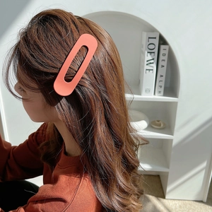 Detail of a large matte orange oval hair clip worn by a model with long brown hair